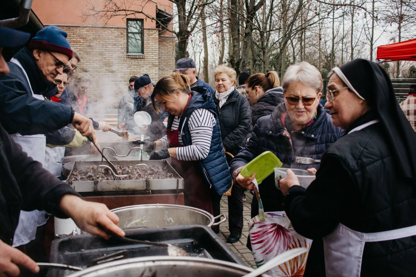 Szabadtéri közösségi főzés, önkéntesek ételt osztanak a sorban állóknak