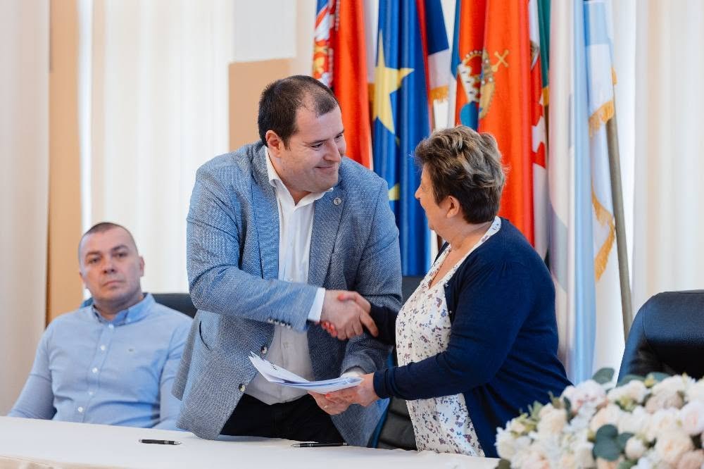 Fejsztámer Róbert kezet fog egy támogatottal a mezőgazdasági támogatási szerződések aláírásán, a háttérben zászlók